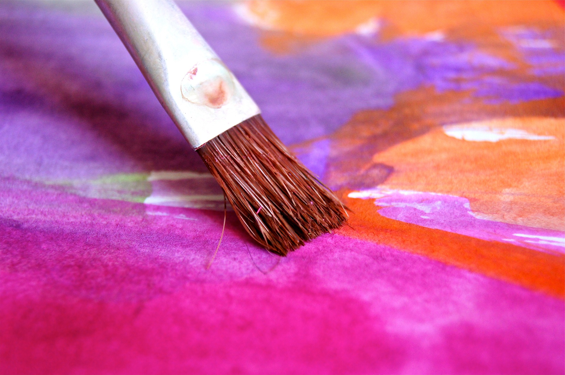 A closeup shot of a paintbrush on an easel painting oranges and pinks
